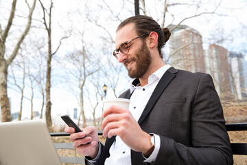 Smiling young businessman with coffee to go looking at cell phone, New York City, USA