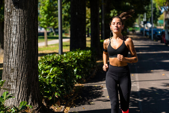 Portrait of young woman running on a tree-lined road
