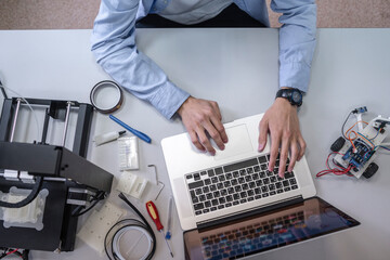 Student setting up 3D printer,using laptop, overhead view