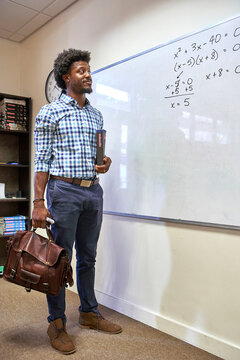 Maths teacher with his bag and his maths book in front of the whiteboard