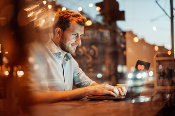 Smiling businessman working on laptop while sitting at cafe