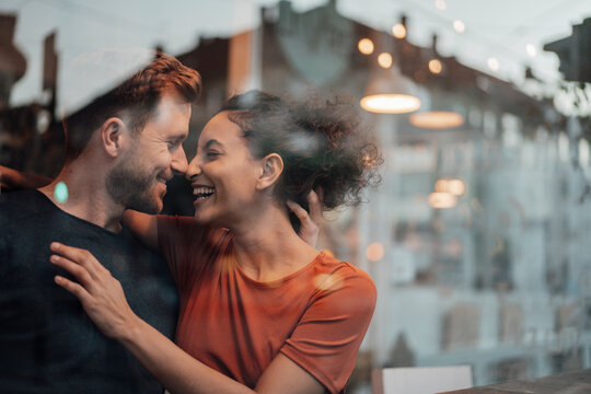 Smiling couple rubbing noses while sitting by cafe window