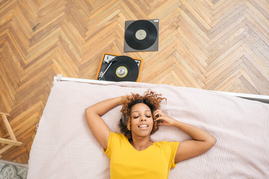 Young woman lying on bed listening to music with headphones and record player