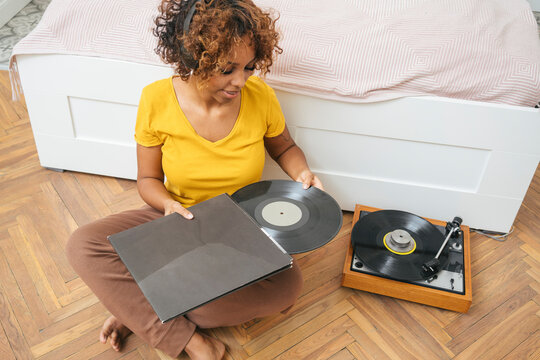 Young woman listening to music with headphones and record player at home