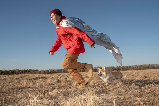 Boy dressed up as superhero running with dog in steppe landscape