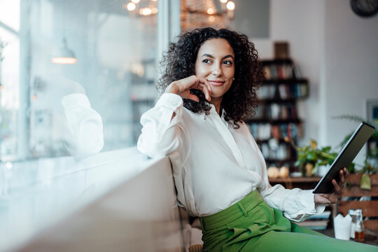 Thoughtful businesswoman with digital tablet looking away while sitting at cafe