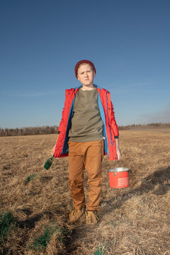 Serious boy with paint bucket and brush in steppe landscape