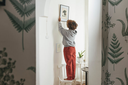 Young woman hanging up picture at home