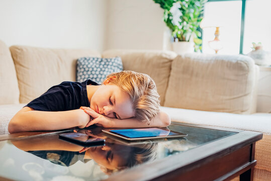 Boy lying on coffee table with smartphone and tablet taking a nap