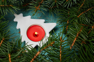 New Year composition from a figurine of Christmas tree with a lit candle on a blue paper background surrounded by fir branches