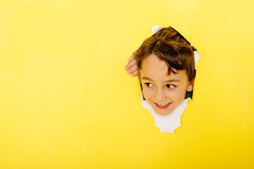 Smiling cute boy tearing yellow paper while looking away