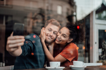 Boyfriend taking selfie with girlfriend through mobile phone while sitting at cafe