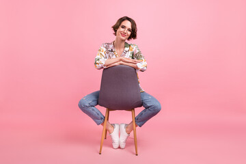 Full length body size photo woman sitting on chair wearing stylish outfit isolated pastel pink color background