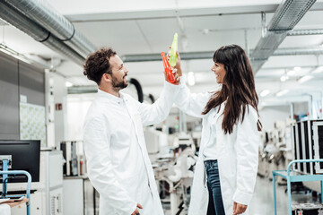 Happy male and female technicians toasting drinks while standing in laboratory