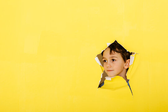Close-up of cute boy looking away through torn yellow paper