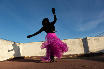 Mujer rebelde irreconocible con elegante vestido de fiesta rosa y abrigada  bailando en la azotea a...