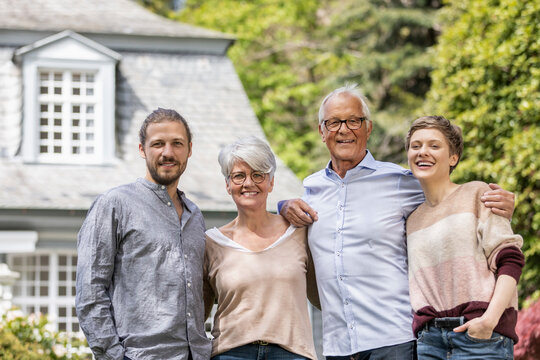 Happy senior couple with adult children standing in garden of their home