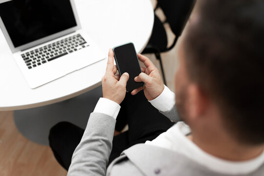 Businessman With Laptop Using Smart Phone In Office