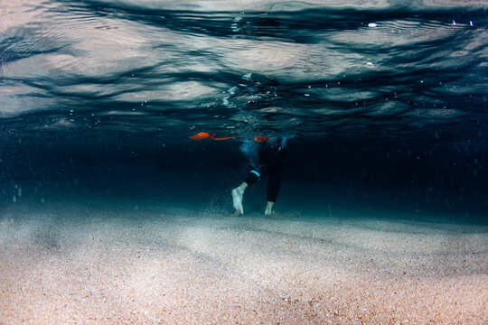 Underwater view of legs of man walking on sandy sea bottom