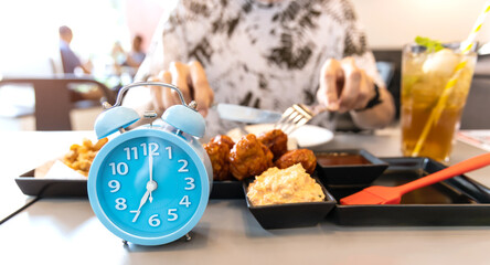 Obraz na płótnie Canvas Selective focus of Blue clock which young man eating food for intermittent fasting in his dish on a table at home