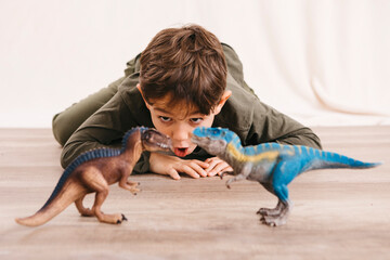 Portrait of little boy crouching on the floor playing with toy dinosaurs