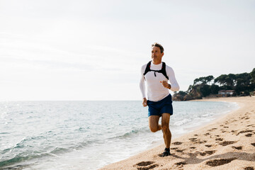 Mature man running on beach during sunny day
