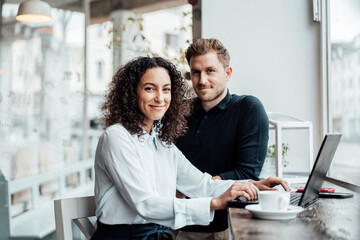 Confident businesswoman sitting by colleague with laptop at cafe