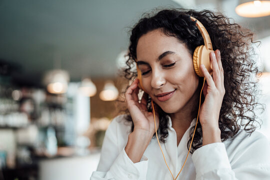 Smiling businesswoman listening music through headphones while standing at cafe