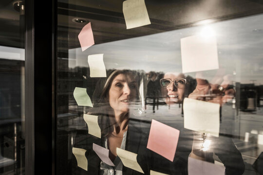 Two businesswomen brainstorming, putting sticky notes on window pane