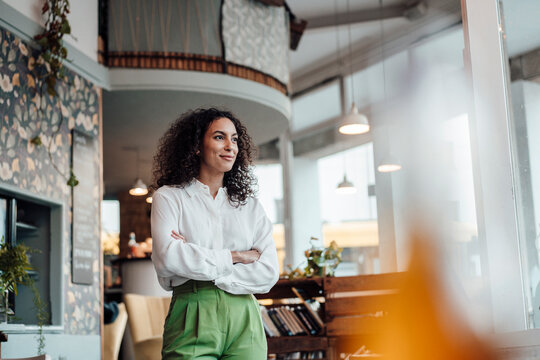 Thoughtful businesswoman looking away while standing with arms crossed at cafe
