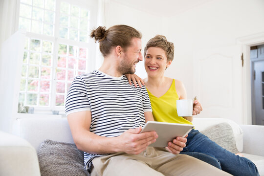 Happy young couple using tablet on couch at home