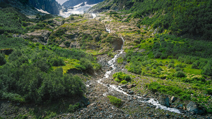 A bottom view of a waterfall flowing from a glacier in a mountain gorge. Mountain river in the Caucasus. Picturesque summer mountain landscape.