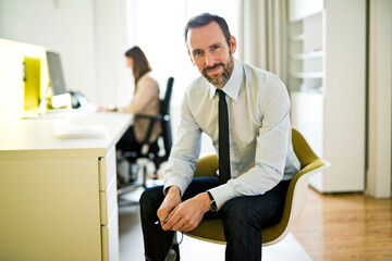 Portrait of confident businessman in office with employee in background
