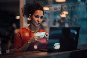 Young woman with coffee cup working on laptop while sitting at cafe