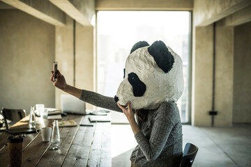 Woman with panda mask sitting in office, taking selfie