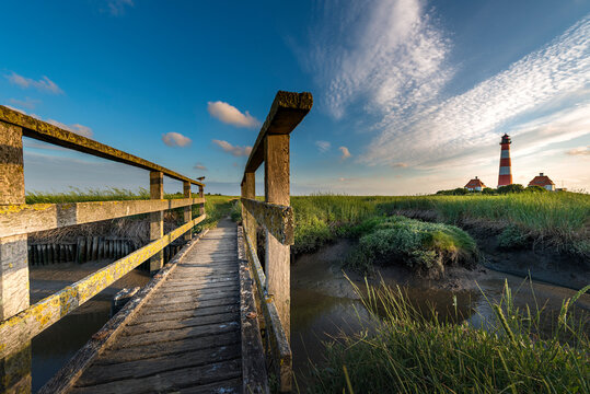 Germany, Westerhever, wooden bridge and lighthouse in sunset