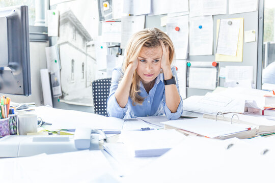 Despaired woman sitting at desk in office surrounded by paperwork