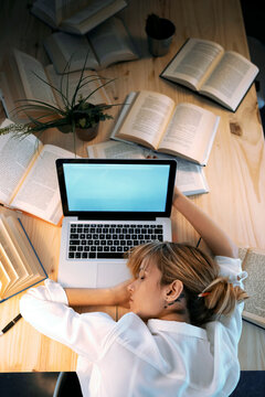Tired woman sleeping over table by laptop and books at home