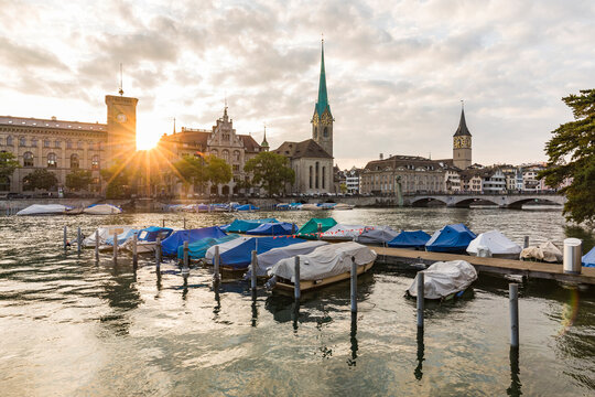 Switzerland, Canton of Zurich, Zurich, Covered boats moored on river Limmat at sunset with old town waterfront in background