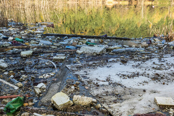 heaps of construction waste, household waste, foam and plastic bottles on the shore of a forest lake, environmental pollution problems