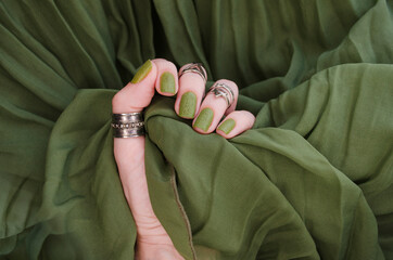 Closeup top view of beautiful painted in green nails isolated on green fabric background. Winter autumn nail style concept.