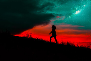 Silhouette of woman walking uphill alone in the night with detail from the milky way and stars...