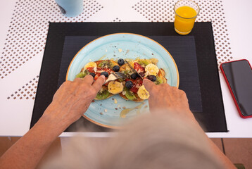 Close-up on woman's hands holding cutlery ready to eat an healthy breakfast, classic american pancakes with banana, kiwi, strawberry and honey. Orange juice on the table