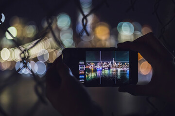 Close-up of woman taking smartphone picture of skyline at night, Manhattan, New York City, USA