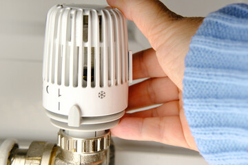 woman regulates the temperature in the house with a thermostat on the white radiator, close-up...