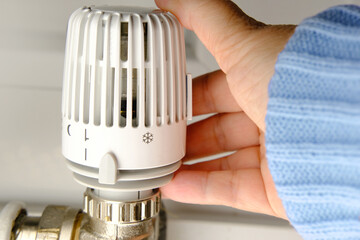 woman regulates the temperature in the house with a thermostat on the white radiator, close-up female hand, concept of saving heat, the beginning of the heating season, shallow depth of field focus - obrazy, fototapety, plakaty