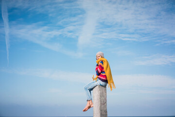 Mature woman sitting on a wood pole on the beach