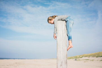 Little girl on the beach hanging on a pole