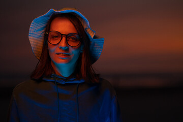 a European woman illuminated by neon light in a hat against the background of the sunset sky. neon...
