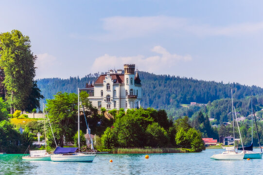 Sailboats moored at lake by church in Woerthersee against sky